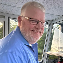 a man wearing glasses and standing in front of a window